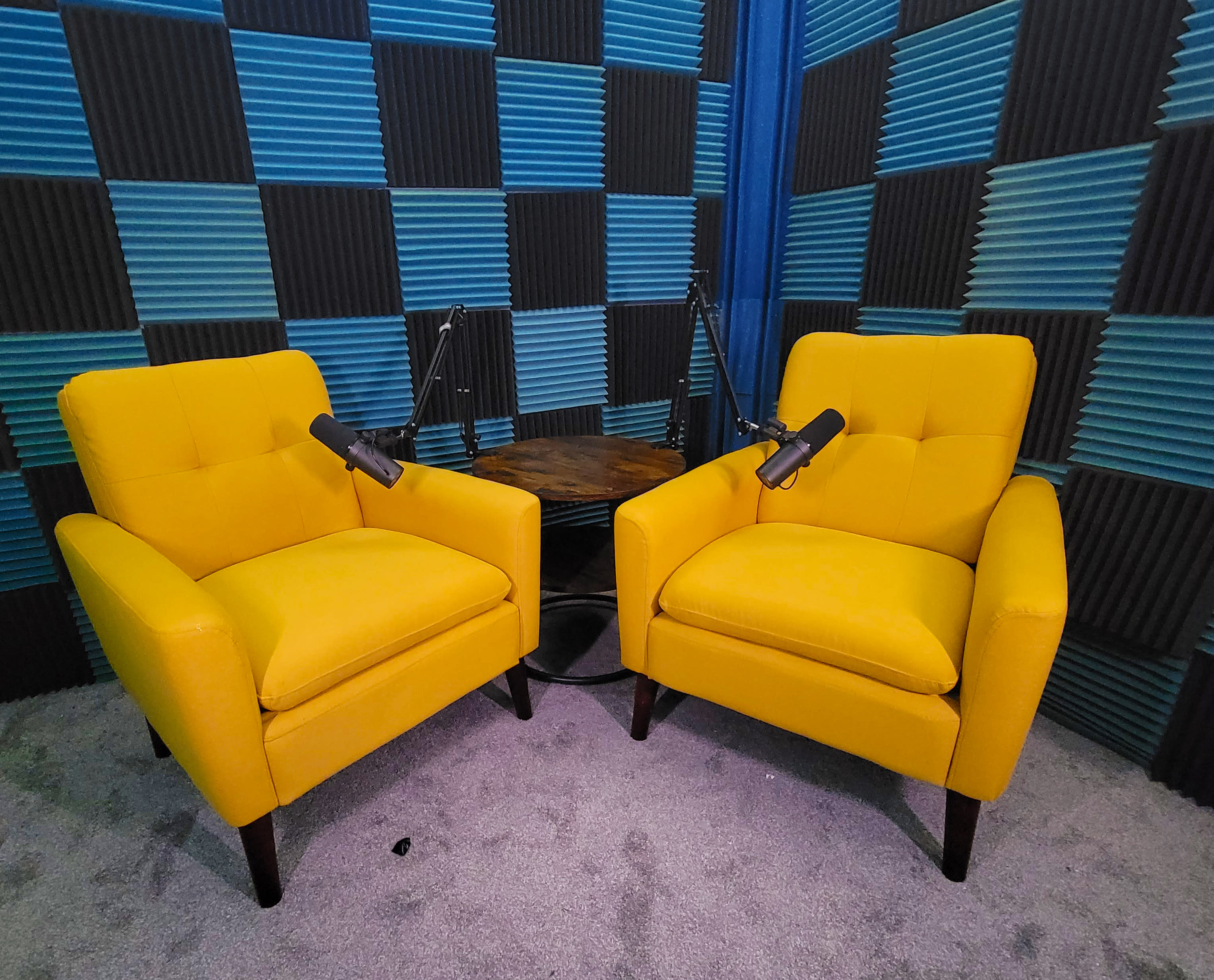 Two people are engaged in a podcast recording while seated in yellow chairs, with microphones positioned in front of them.