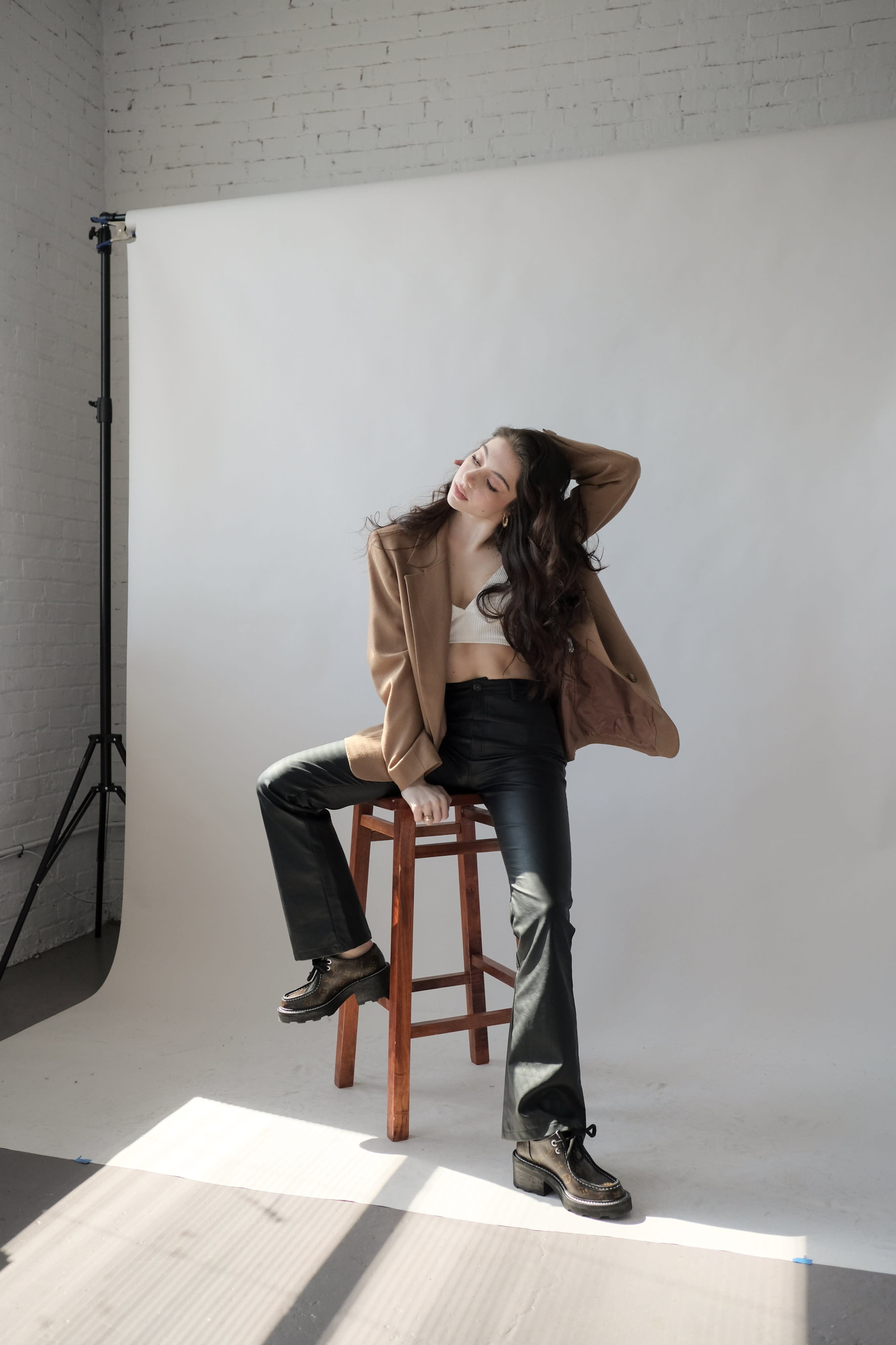 A photographer captures a model posing on a chair against a backdrop of sunlight streaming through large windows.