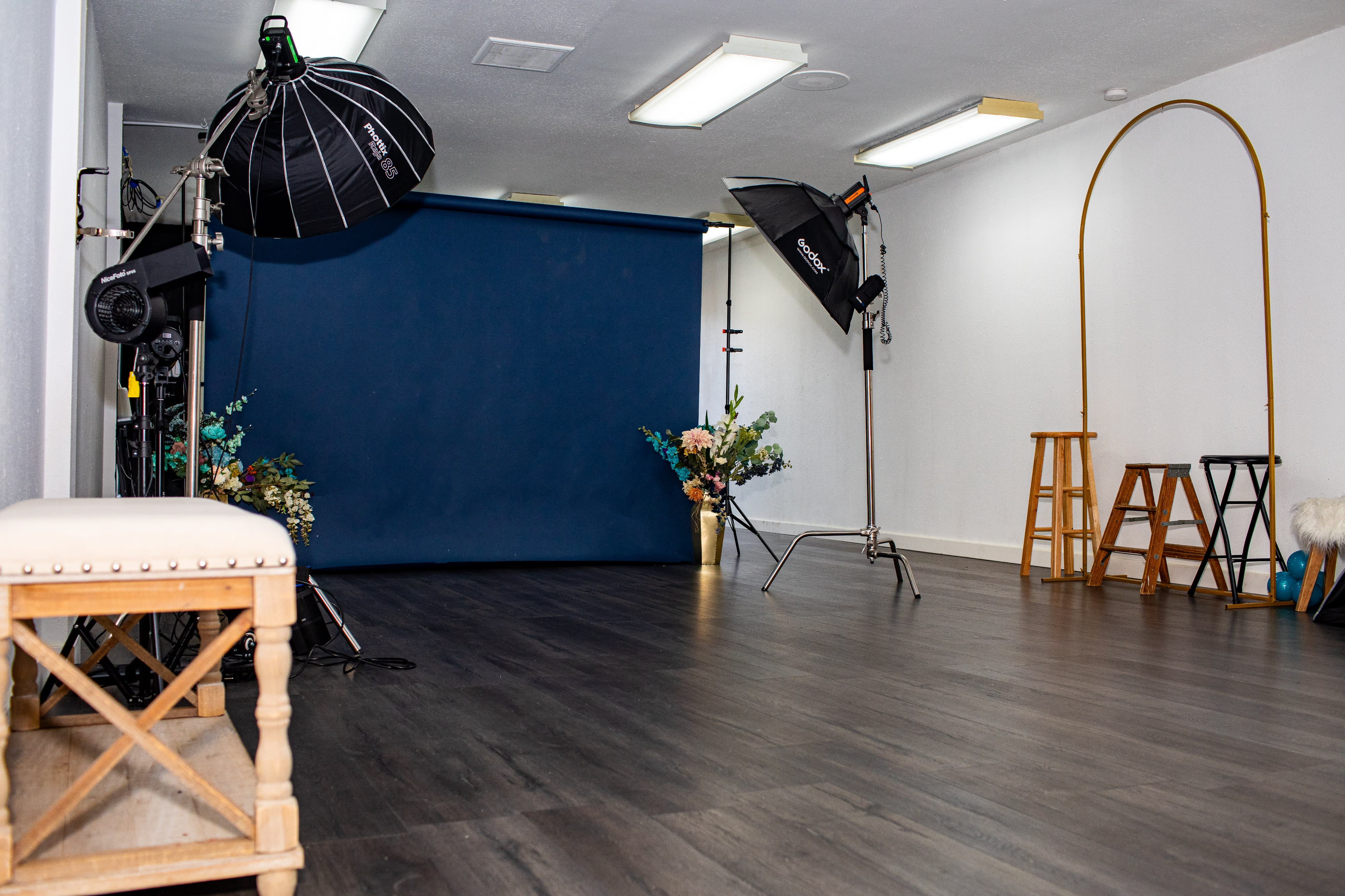 A photography studio set up with a bouquet of flowers on a backdrop, a stool in front, and various equipment scattered on the floor.