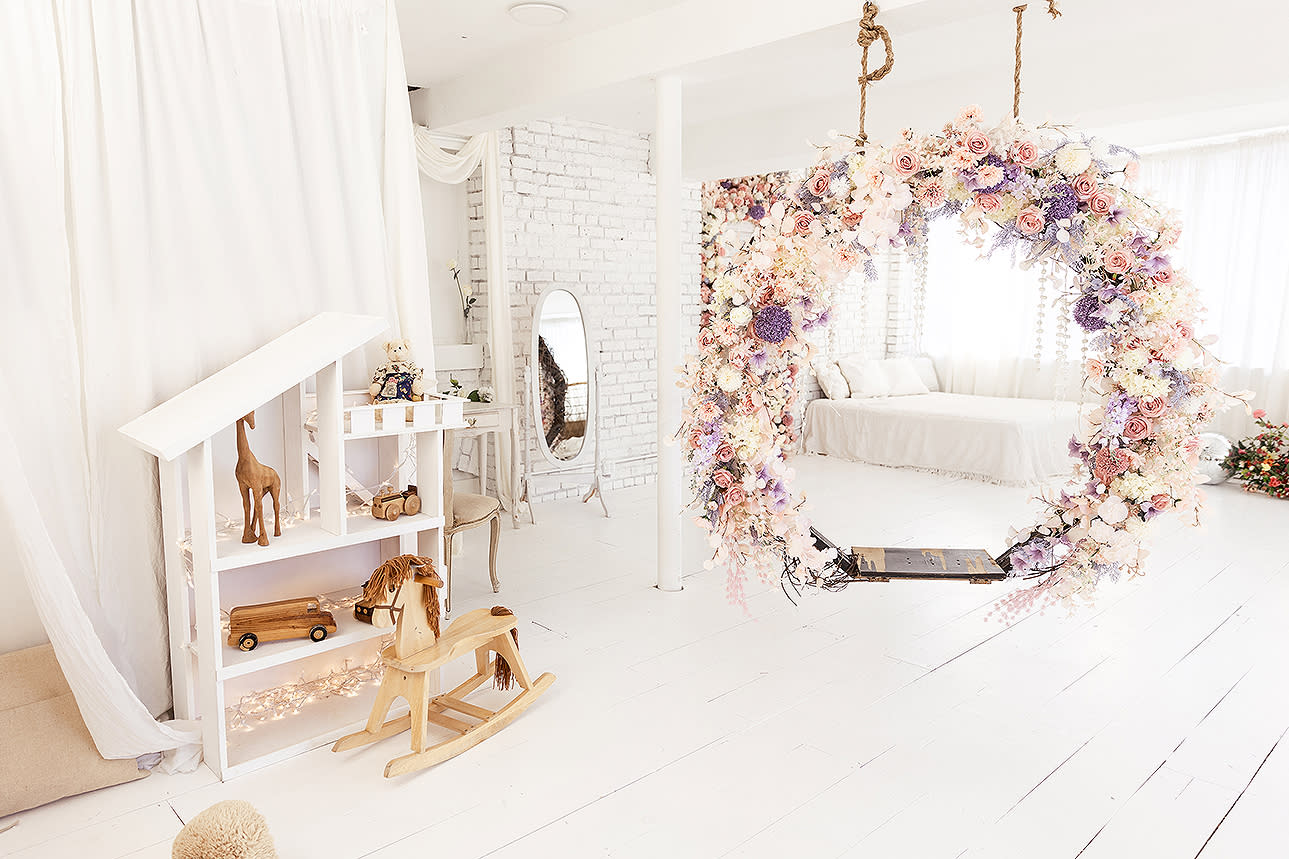A baby smiles while riding a wooden rocking horse in a decorated room with a Christmas tree and an assortment of toys.