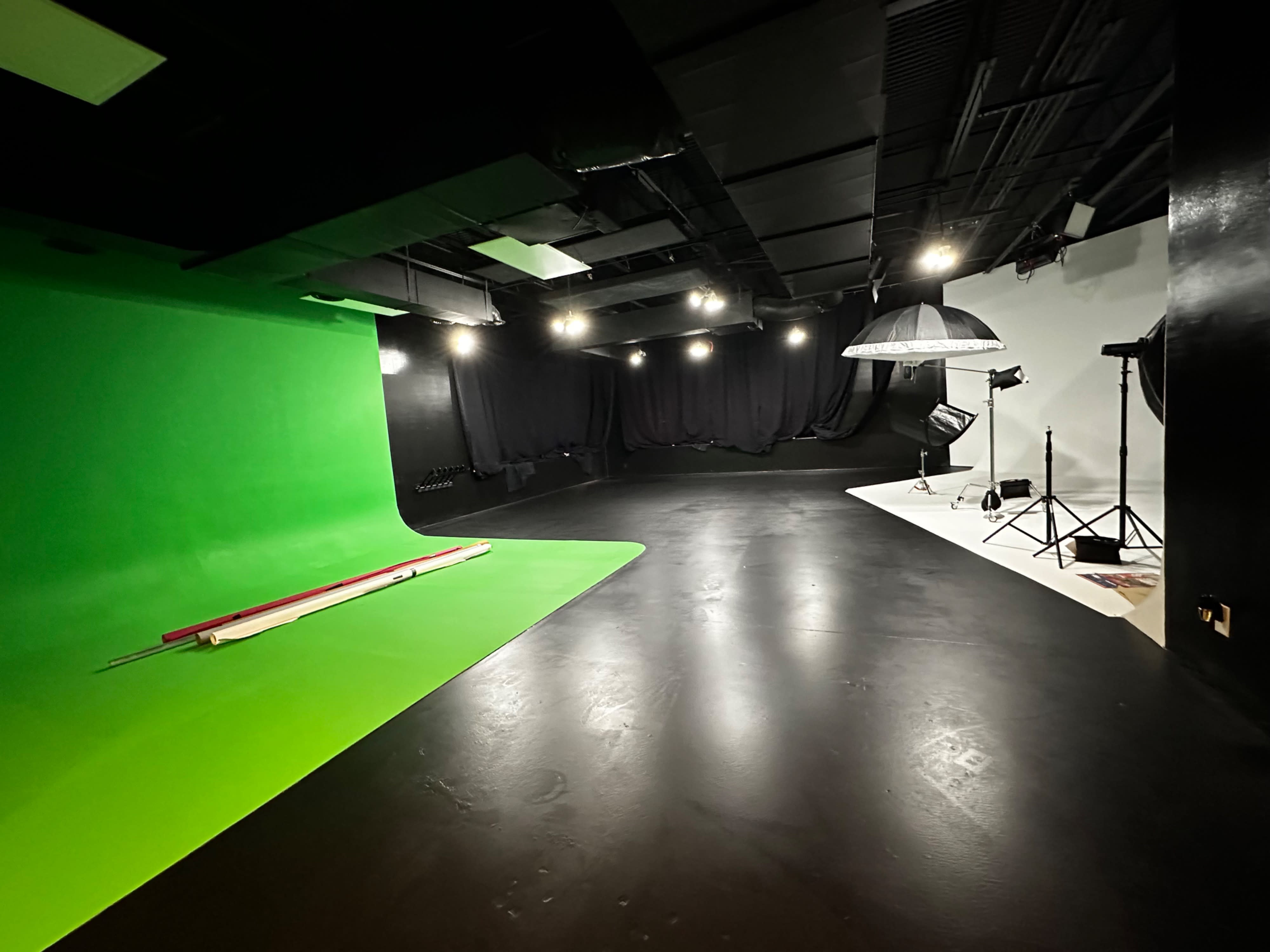 A performer in scrubs stands microphone in hand against a green screen backdrop during a video shoot.