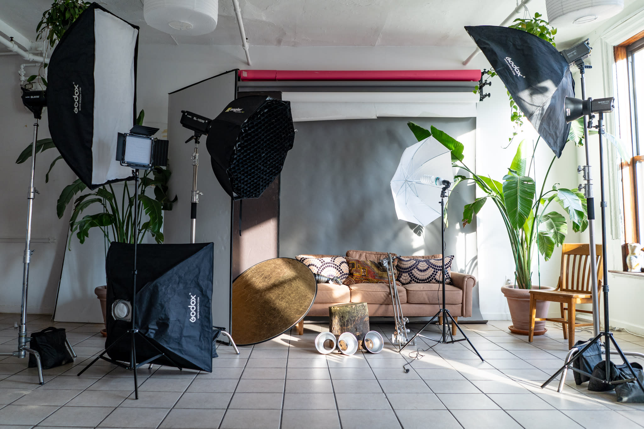 A photographer adjusts equipment while a model poses on a wooden chair against a backdrop in a studio.