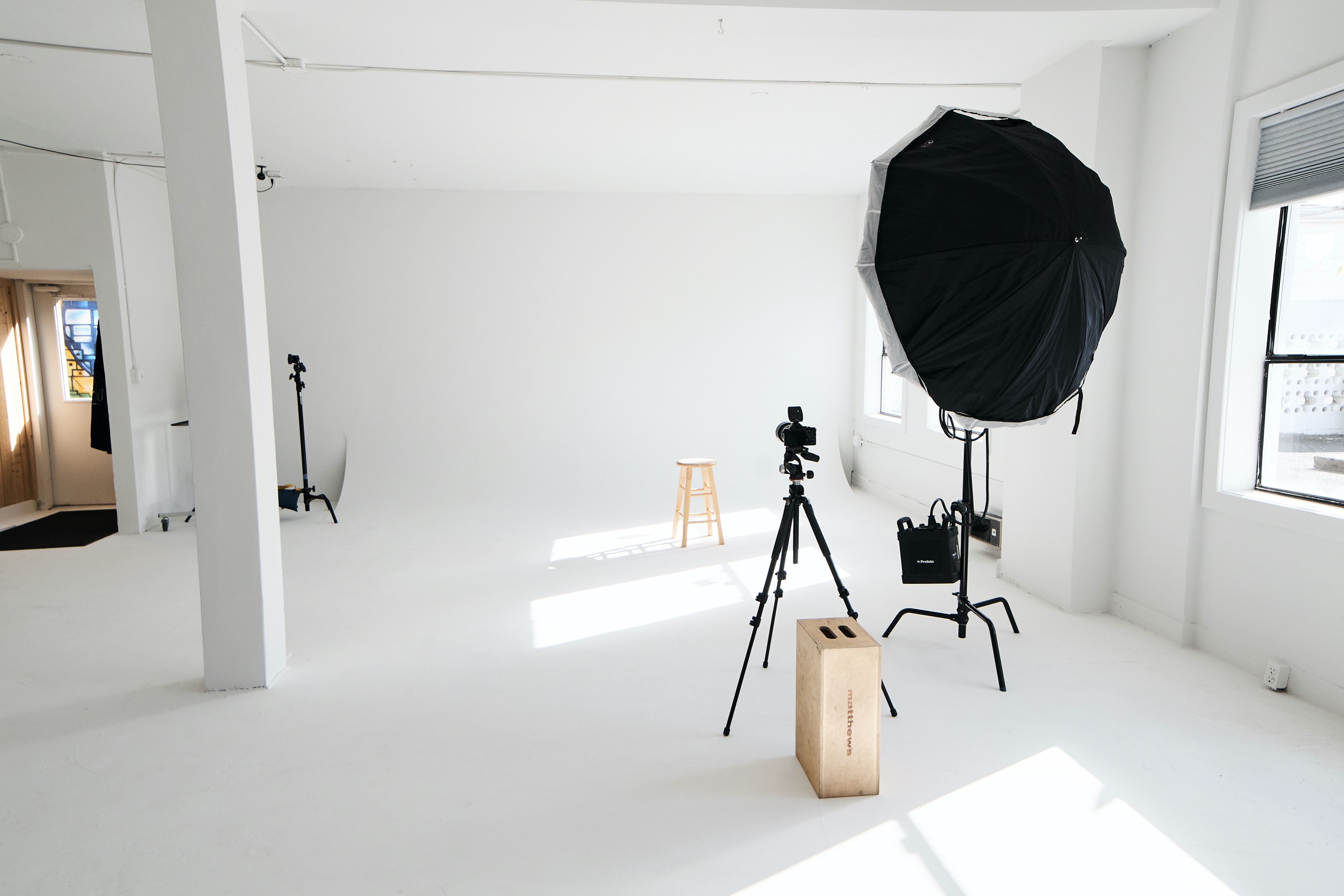 A person operates a video camera in a minimal studio space equipped with various filming equipment.
