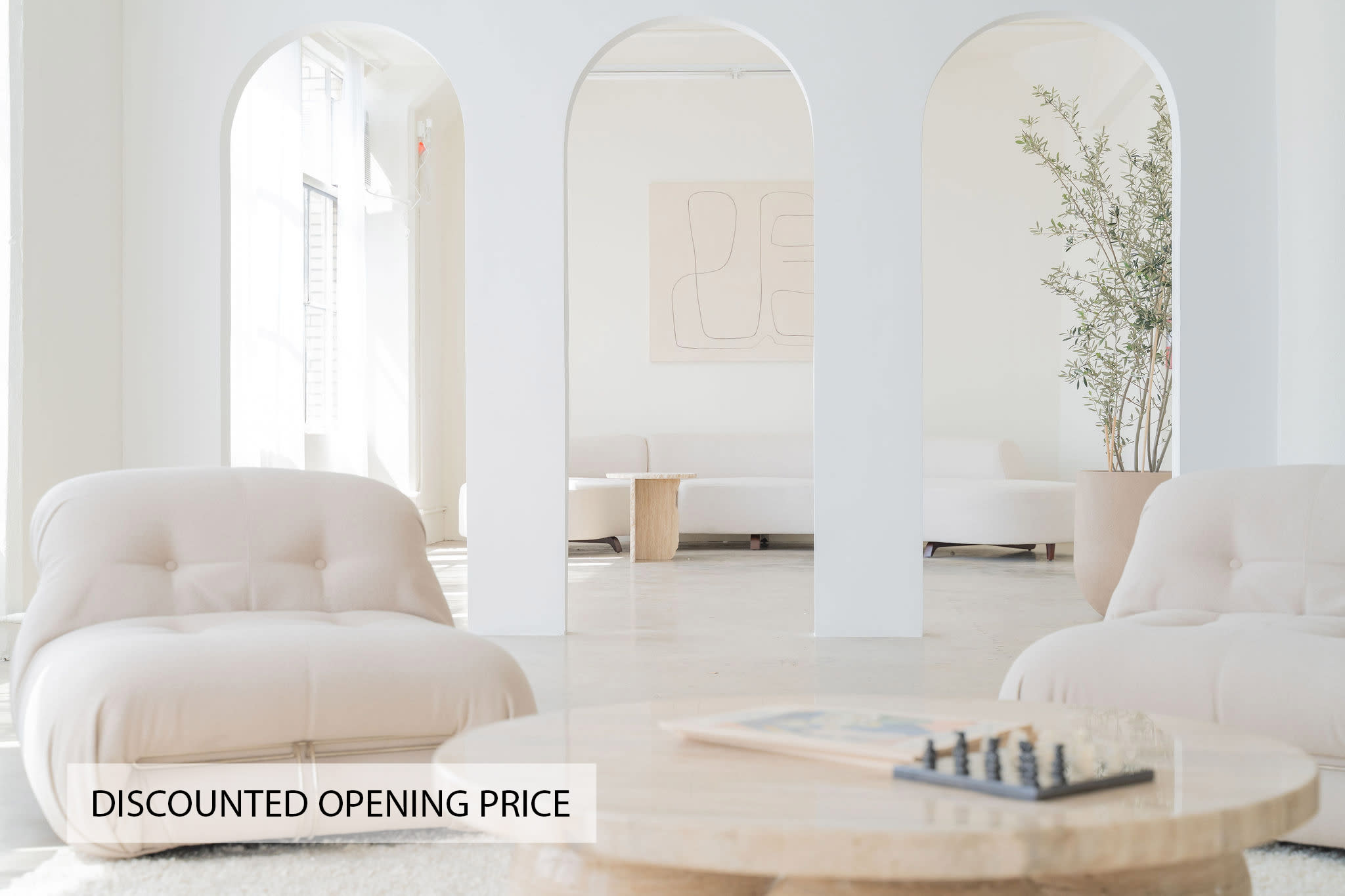 A well-lit photography studio features a beige sofa, wooden tables, and a decorative mirror, with sunlight streaming in through large windows.
