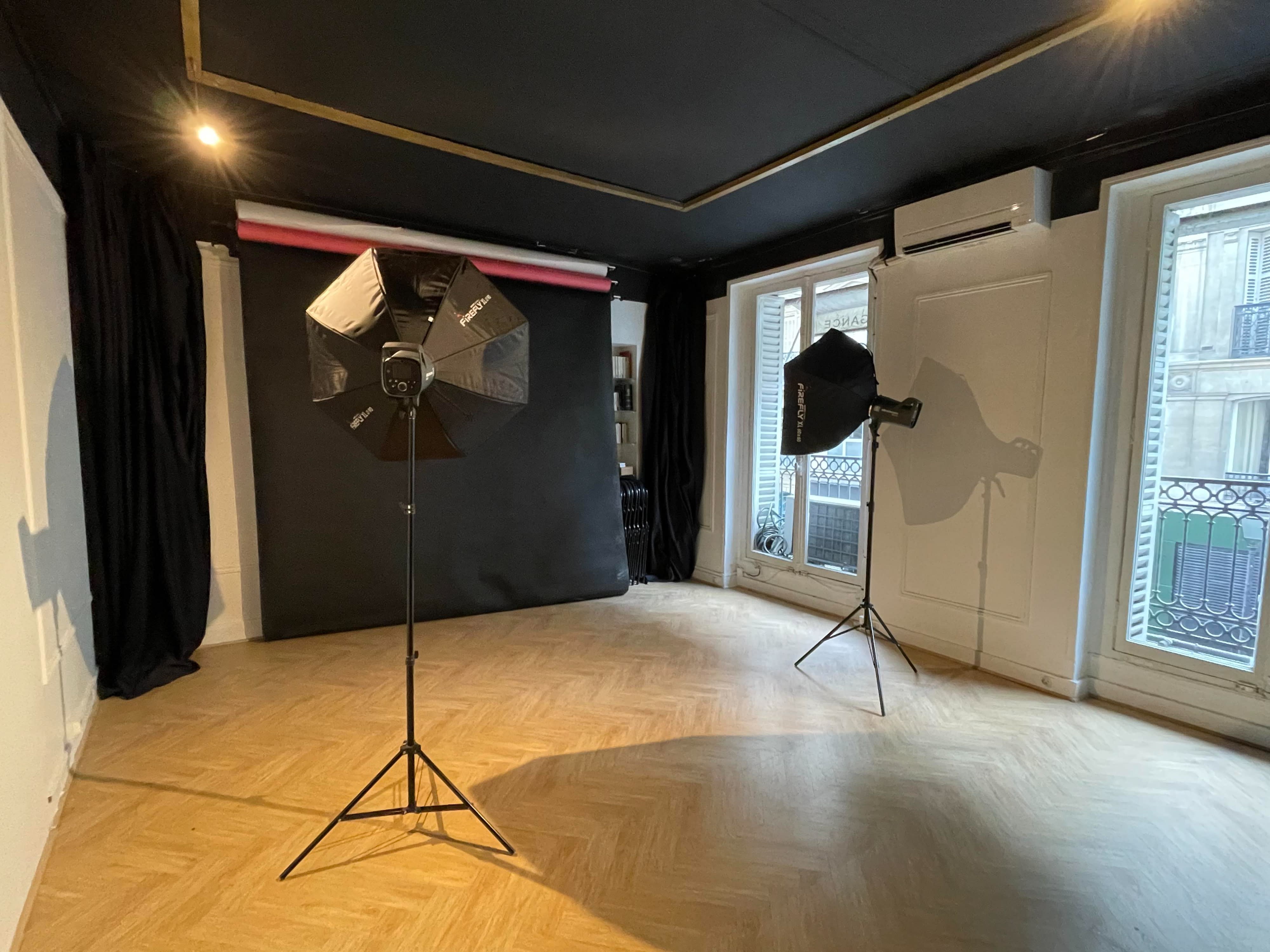 A person in a black t-shirt holds two drinks while another individual captures the photo with a camera in a studio setting.