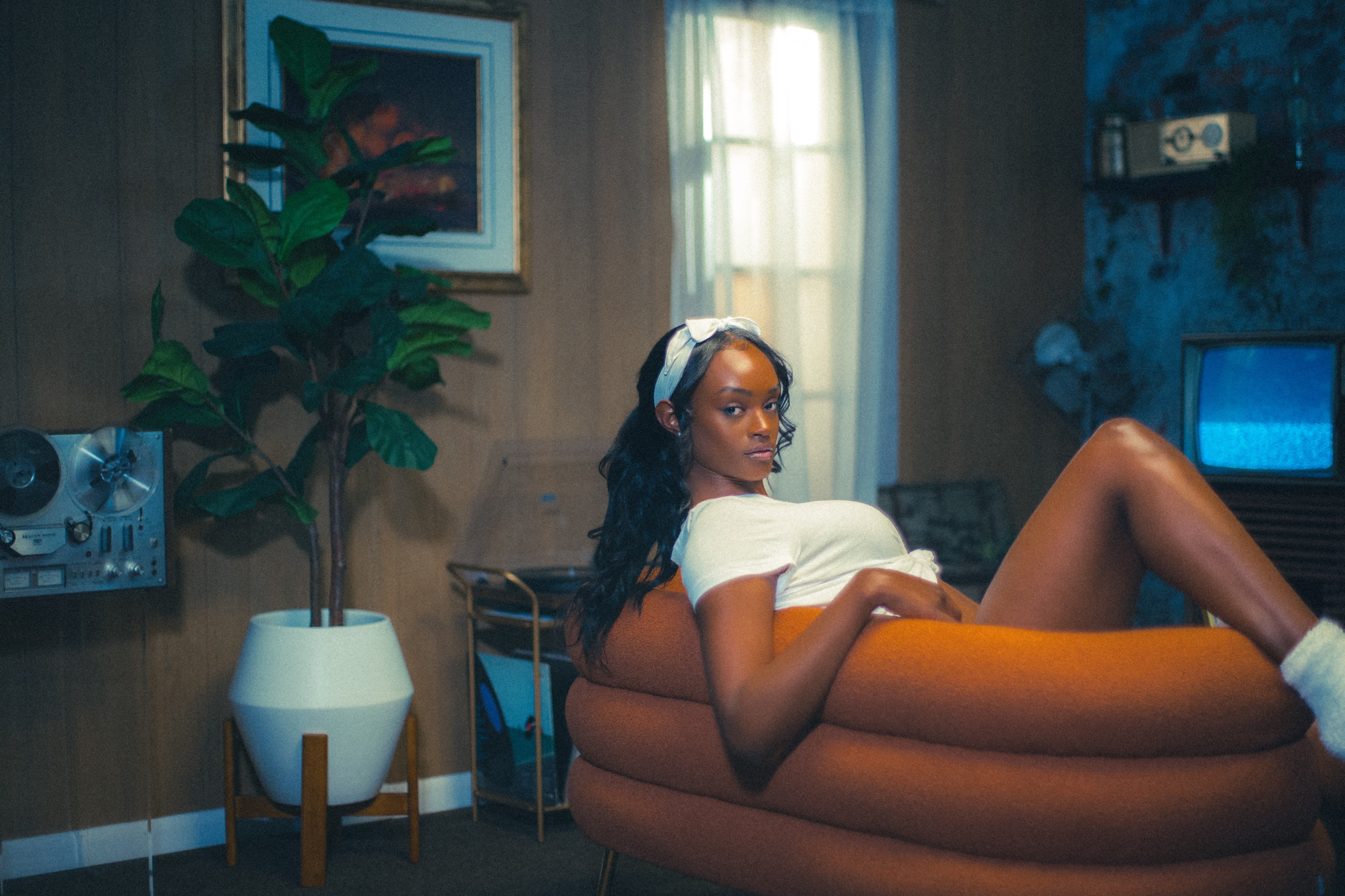 The scene features a photoshoot with two models reading books, one sitting in front of a plant while the other is positioned in the background.