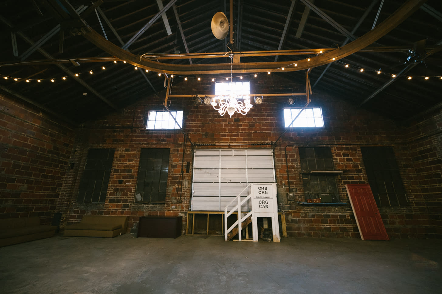 A person sits on a chair under a large professional lighting setup in an industrial space during a video shoot.