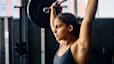 A woman doing an overhead press with a barbell in the gym.