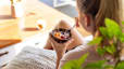 A runner eating a yogurt parfait with fruit after a run while sitting on the couch at home.