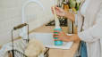 A woman cleaning a water bottle using a brush in the kitchen sink.