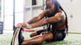 Young woman stretching to build muscle in a gym setting.