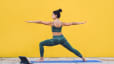 Side view of focused calm female in sportive outfit concentrating in warrior pose on yoga mat with yellow background behind