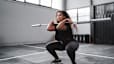 Woman does a squat with a barbell bar without weights, a beginner barbell exercise