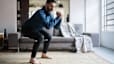 A middle-aged man performing a squat exercise while following a guided workout at home.