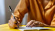 A close-up photo of a woman journaling for mental health with a small notebook and a pen.