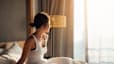 A woman waking up early. She's sitting up in bed and looking out the window.