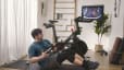 Man does a core exercise on the mat next to Peloton Bike. 