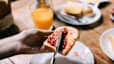 A person spreading jam on a piece of toast next to a glass of orange juice. This meal would make an ideal breakfast before a marathon.