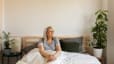 A calm woman sitting in bed practicing mindfulness and looking to her left as she focuses on how to be more present in her daily life.