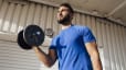 A man lifting a dumbbell while standing near a wall. Learn if working out increases testosterone in this article.