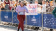 A woman happily running a marathon while a spectator behind her holds up a marathon sign that says "We believe in you!"