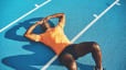 A male athlete experiencing bonking. He is exhausted, lying down on his back with his hands on his head, on a blue track.