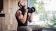 A man sitting down and lifting dumbbells in a sunny, airy gym.