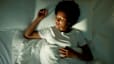 A woman practicing sleep meditation in bed. She's lying on her back under the covers with her eyes closed.