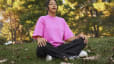 A young woman sitting outside in the grass doing a meditation for anxiety.