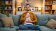 A man sitting on the couch at home with his hands on his chest and belly, practicing a loving-kindness meditation.