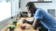 A happy man leaning on his kitchen counter while eating breakfast before a workout.