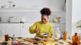 A happy woman at home preparing a healthy breakfast with complex carbohydrates like fruits and nuts.