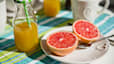 A plate with a grapefruit cut in half next to a bottle of fresh orange juice, both of which are hydrating foods and drinks.