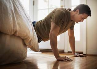 A man doing push-ups before bed. He is in a high plank position next to his bed.