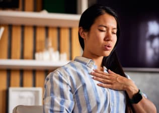 A woman breathing out through her mouth while practicing cyclic sighing. Her hand is resting on her chest.