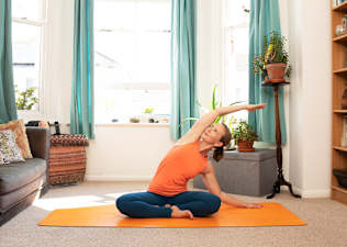 Woman doing seated side bend oblique stretch at home on a yoga mat