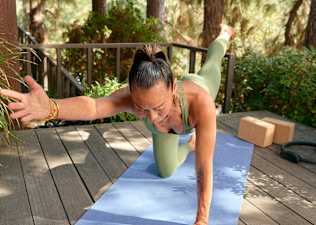 Woman doing the bird dog exercise during a Peloton Pilates class outside on her deck.