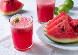 A glass of watermelon juice garnished with fresh mint leaves sitting next to a plate of other watermelon slices.