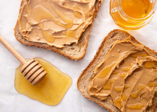 A honey stick sitting near two slices of peanut butter toast that also have honey on them.