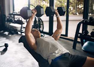 A young man does incline dumbbell chest presses at the gym to build chest muscles