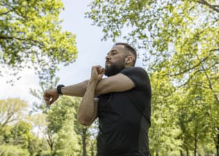 Man doing cross body shoulder stretch outside in park