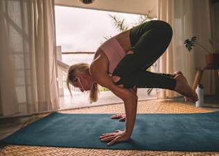 Woman practicing Crow Pose on a mat while doing yoga at home.