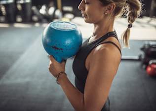 Woman doing the kettlebell halos exercise in a gym with a blue kettlebell.