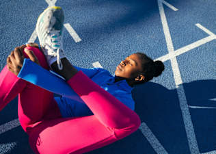 A woman lying down on a blue track and doing a figure 4 stretch.