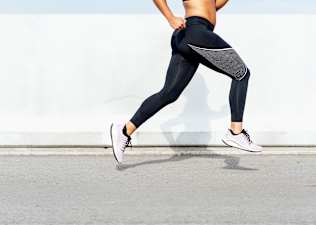Close up shot of a woman's legs while she's running strides outside.