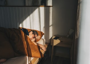 A man who is waking up tired in bed after a full night of sleep. He's lying in a modern-looking bed looking disgruntled.