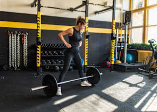 Woman in a gym preparing to do a sumo deadlift with a loaded barbell.