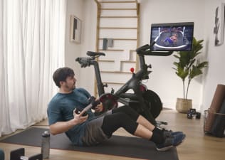 Man does a core exercise on the mat next to Peloton Bike. 