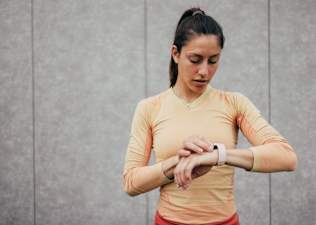 Young woman in fitness gear checking her heart rate zone on a smartwatch during her long run