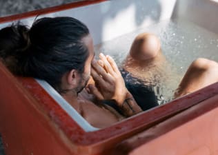 A man taking an ice bath and holding his hands to his face. Learn about cold showers vs. ice baths in this article.